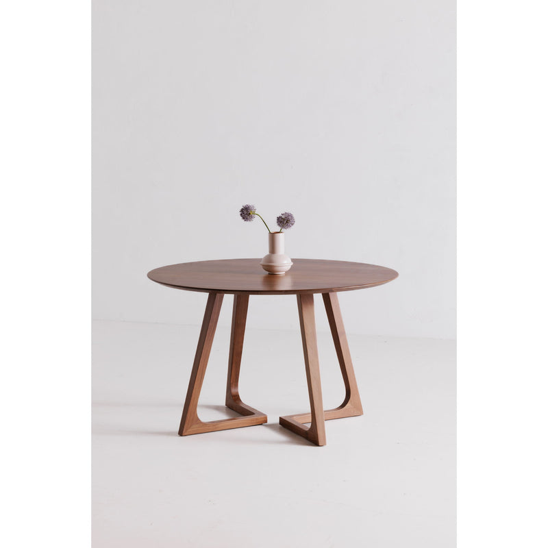 Round walnut dining table with sculpted X-style legs and flower vase centerpiece