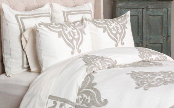 Ivory sham pillow with large gray damask scroll embroidery, shown on a bed