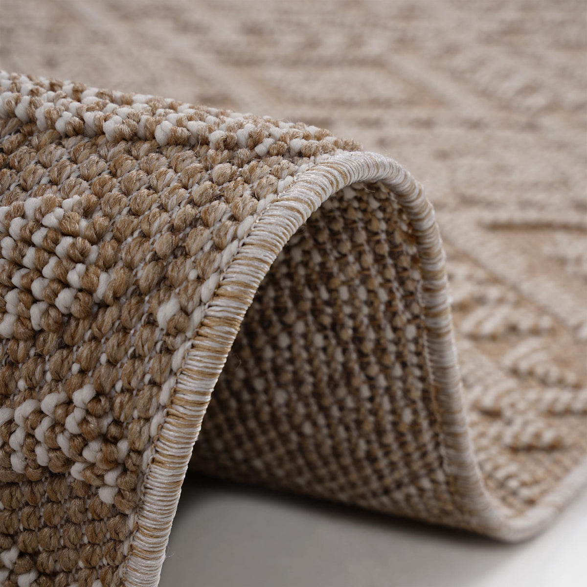 Light brown rug corner close-up with looped texture and light striped fringe trim.