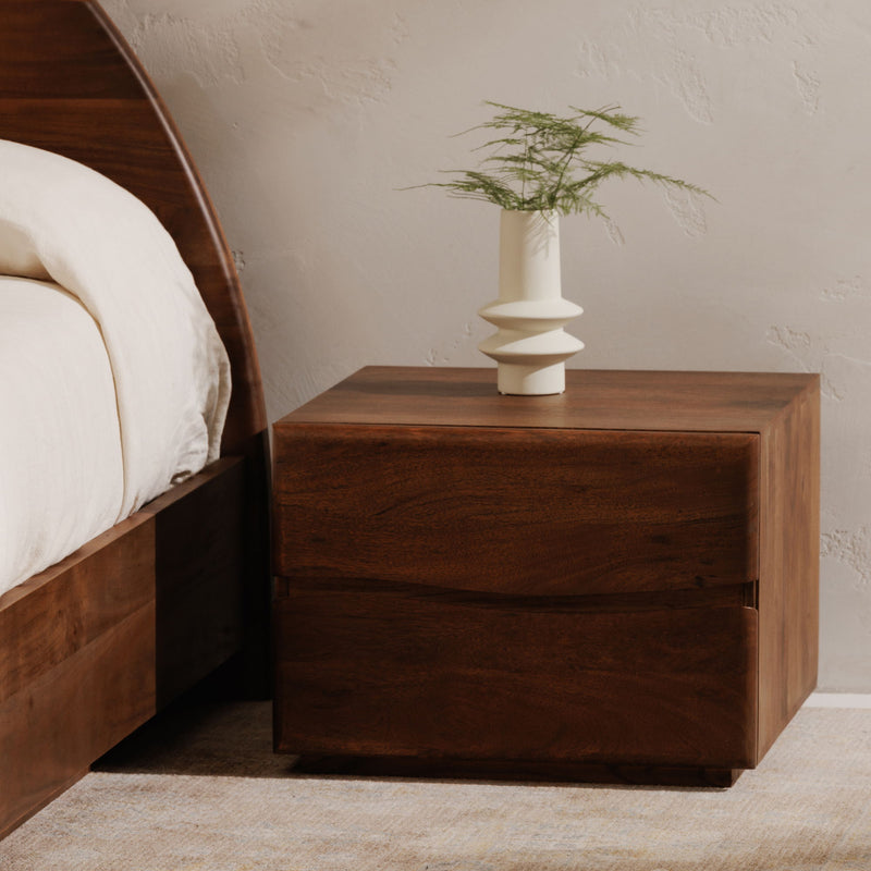 Brown wooden nightstand with single drawer beside a bed