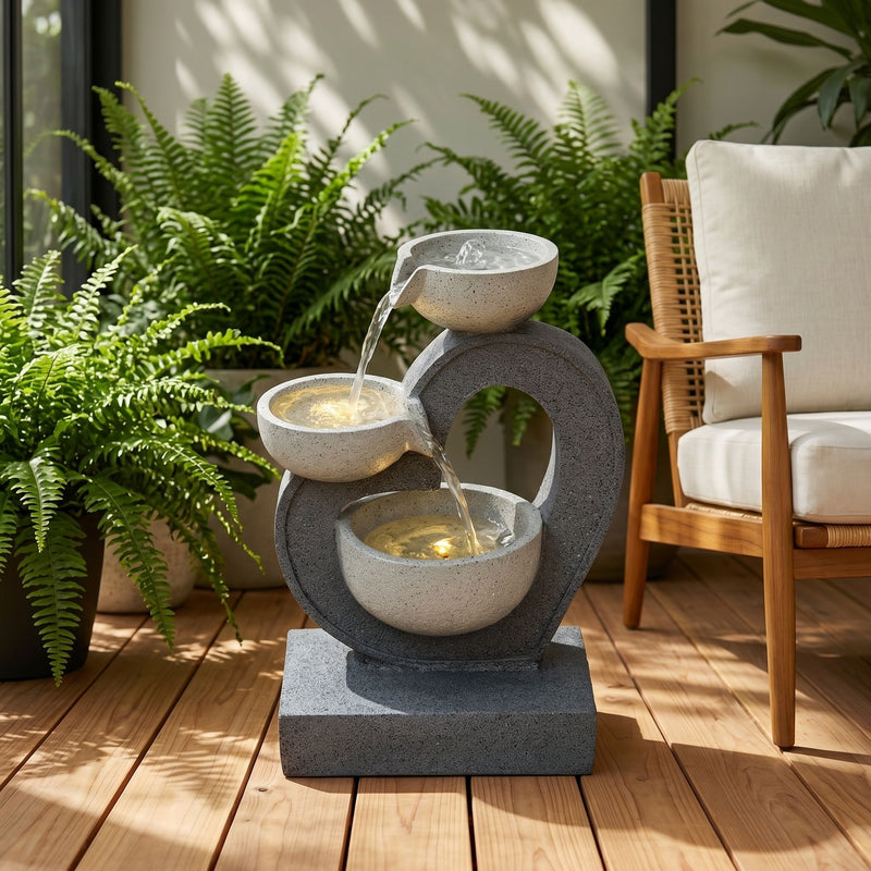 Gray three-tier outdoor fountain with cascading water and warm lights in its bowls