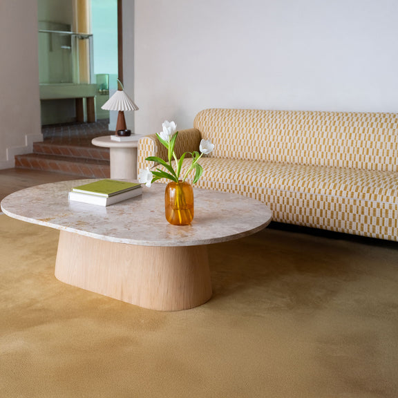 Round coffee table with mottled light stone top and light wood pedestal base