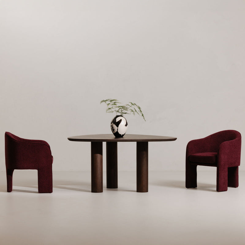 Plum upholstered dining chair with curved back and armrests, shown beside a table