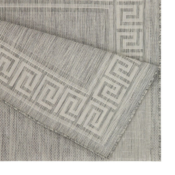 Close-up of light gray area rug corner with Greek key border and woven weave.