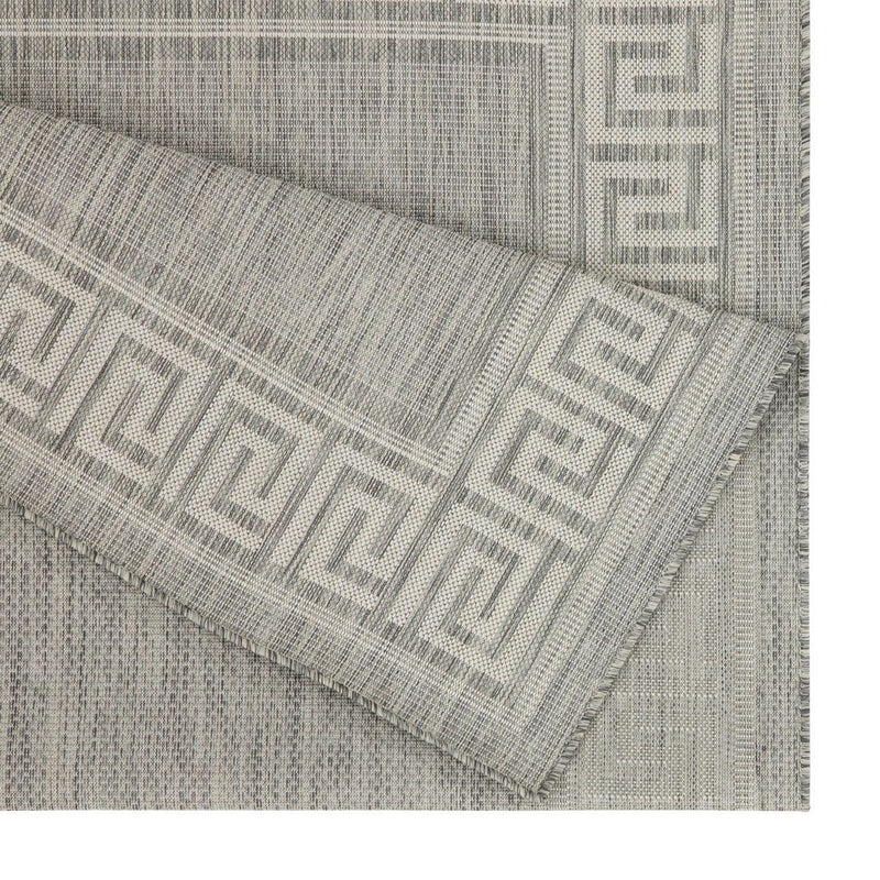 Close-up of light gray area rug corner with Greek key border and woven weave.
