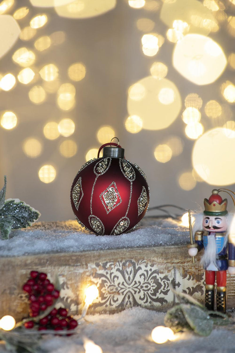 Red and gold Christmas ball ornament on snow with glowing bokeh lights and nutcracker