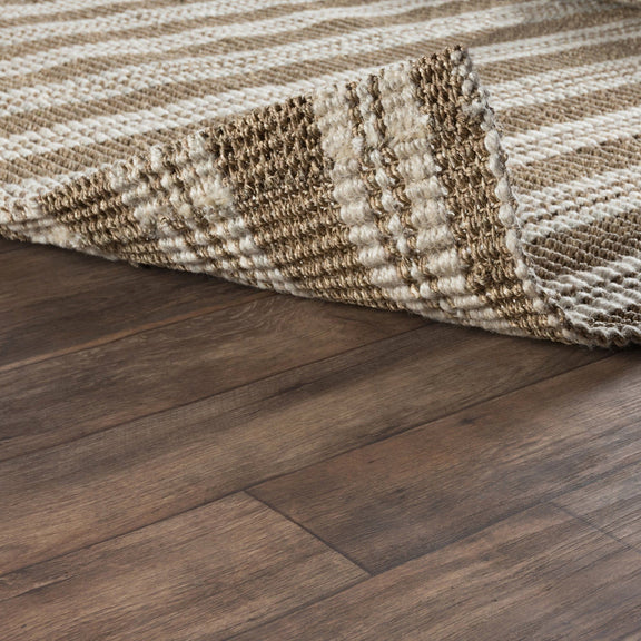 Woven striped area rug edge detail with neutral tones on dark wood floor.