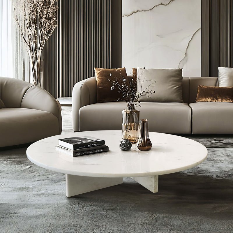 Round white marble coffee table with four-legged stone base and veined surface