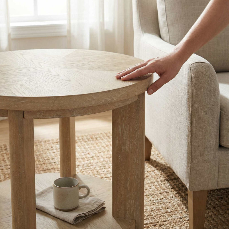 Round light-brown wood coffee table with lower shelf, touched by a hand