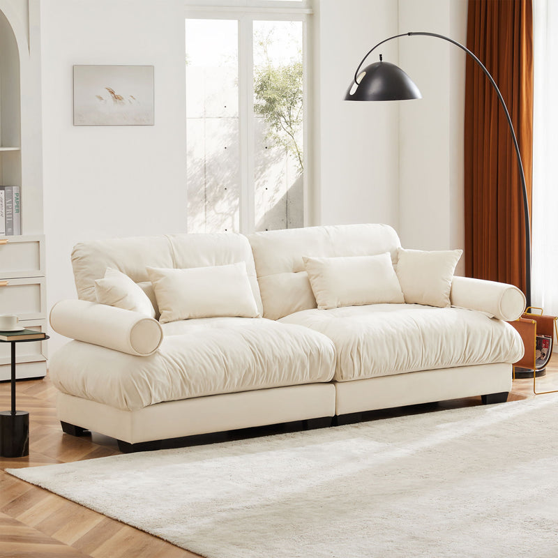 Beige upholstered sofa with tufted cushions, back throw pillows, and rounded bolster arm