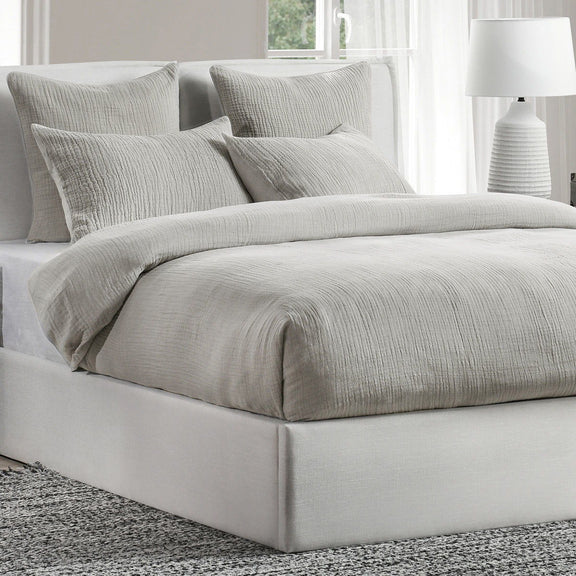 Light gray pillow shams on a bed with boxy, tufted-looking edges and crinkle texture