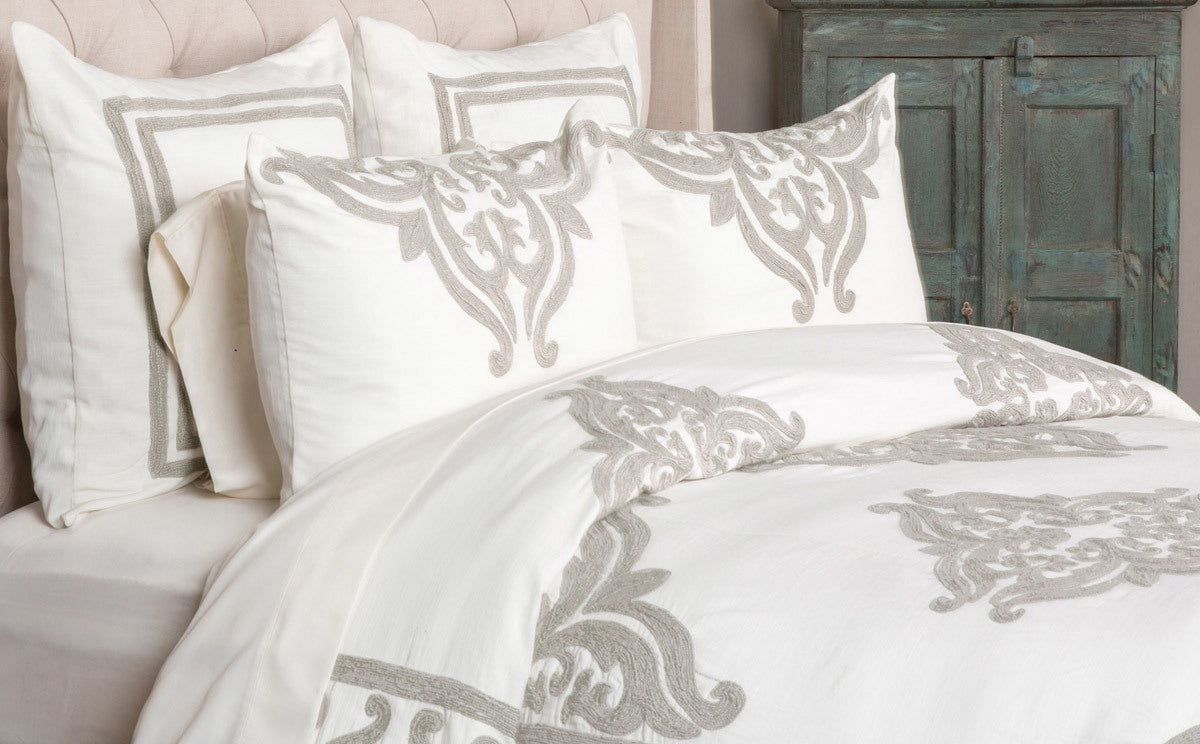 Ivory sham pillow with gray damask scroll ornament at center, on bed