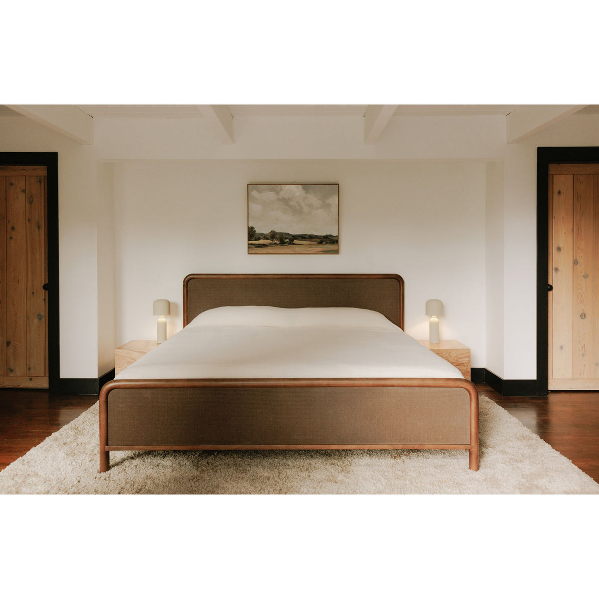 Queen bed centered in room, warm brown frame with upholstered headboard