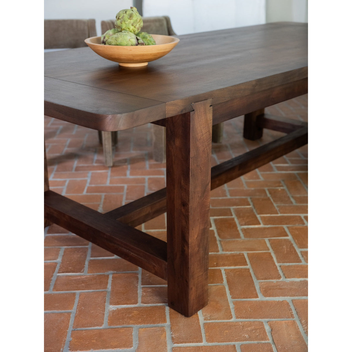 Warm brown dining table close-up with thick tabletop, corner detail, and cross braces.
