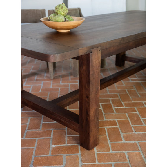 Warm brown dining table close-up with thick tabletop, corner detail, and cross braces.