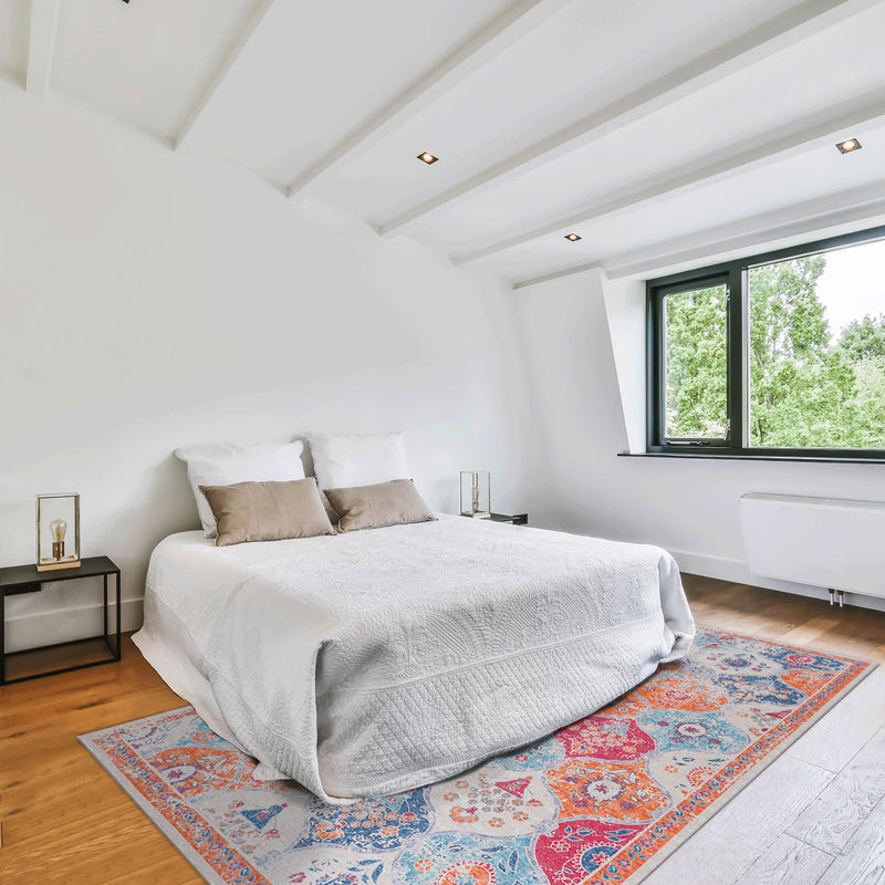 Orange and blue patterned area rug under a bed with a light gray duvet