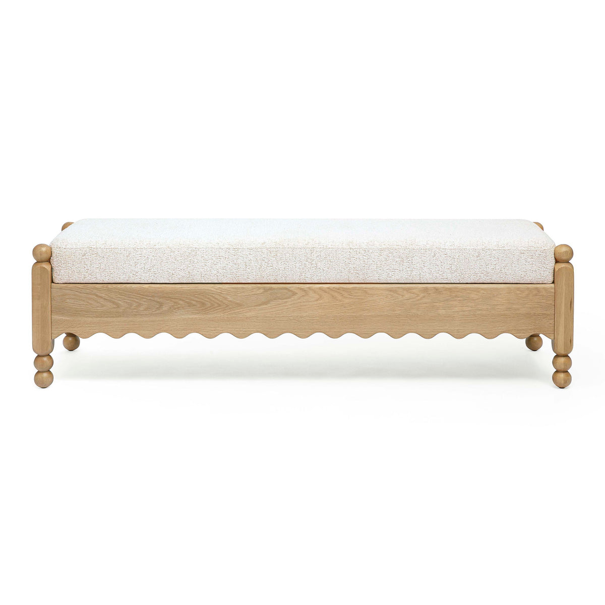 Cream bench with textured upholstery, light wood frame, scalloped apron and round legs.
