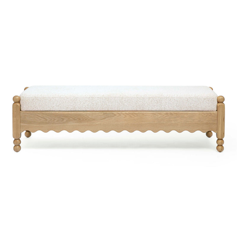 Cream bench with textured upholstery, light wood frame, scalloped apron and round legs.