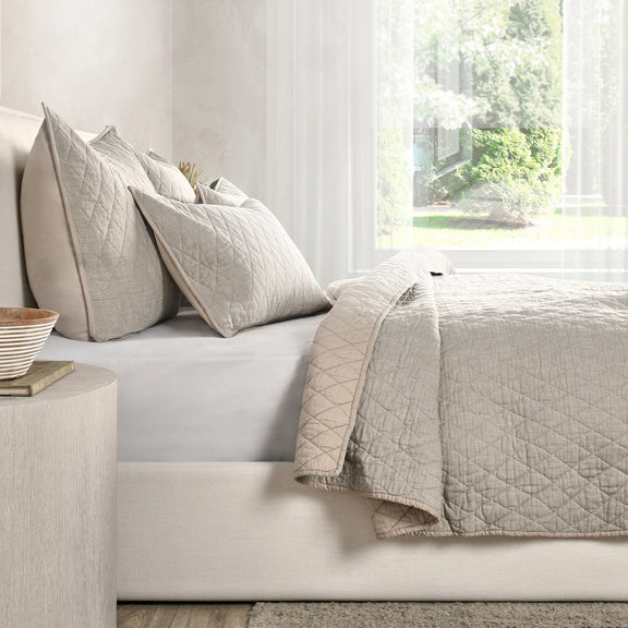 Natural-tone quilt and decorative pillows with diamond quilting on a sofa