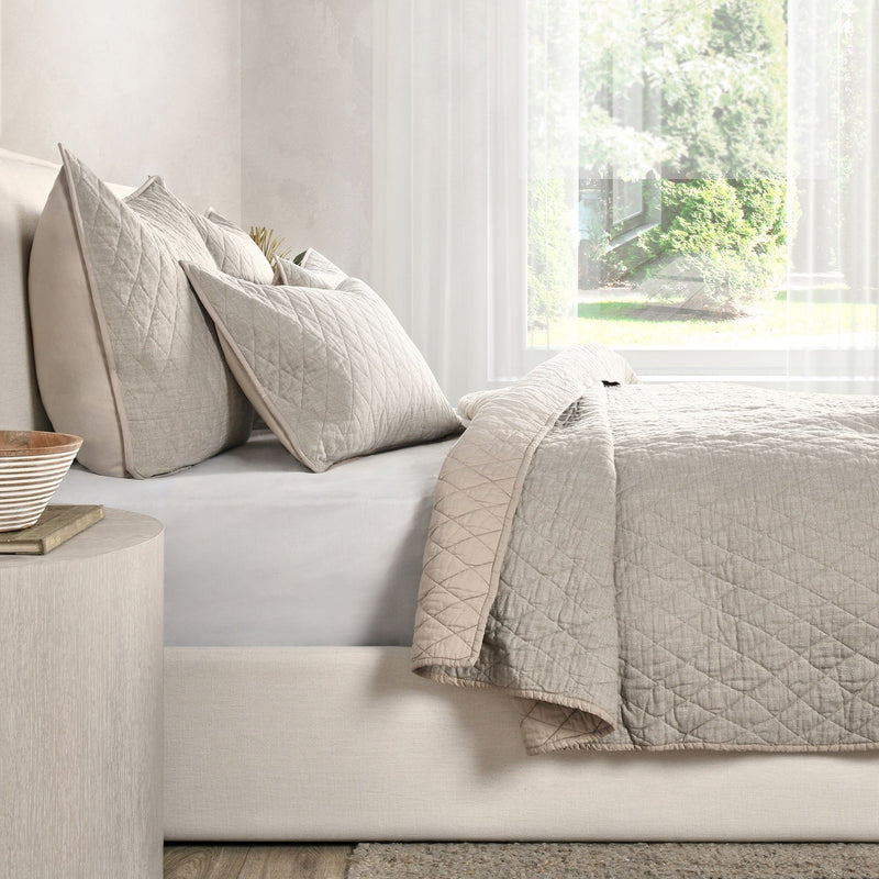 Natural-tone quilt and decorative pillows with diamond quilting on a sofa