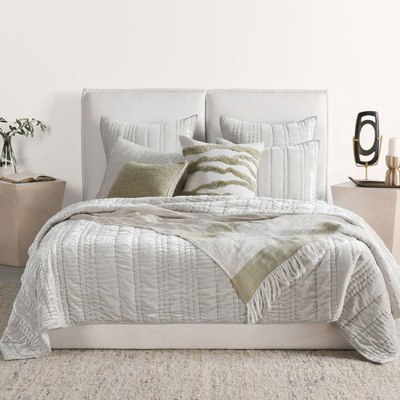Ivory quilt with stitched channel pattern, layered with a green accent throw and pillows