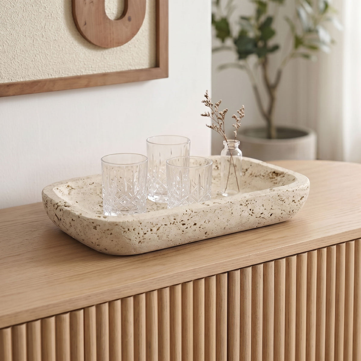 Beige travertine tray holding three glass cups and small stems.
