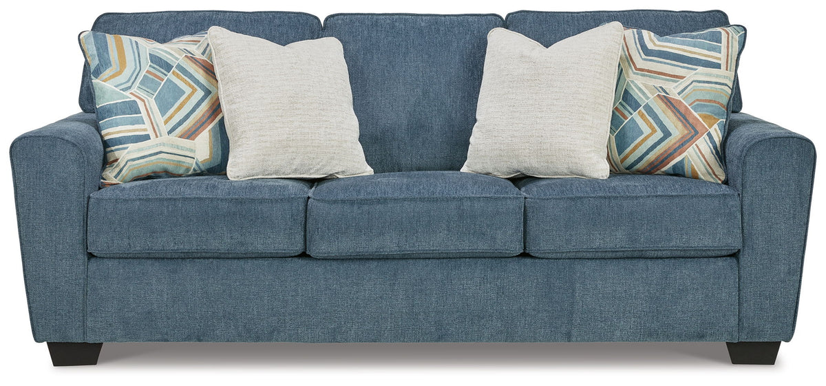 Blue fabric sofa with three seat cushions and four throw pillows, two patterned, two cream