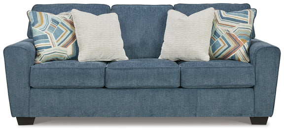 Blue fabric sofa with three seat cushions and four throw pillows, two patterned, two cream