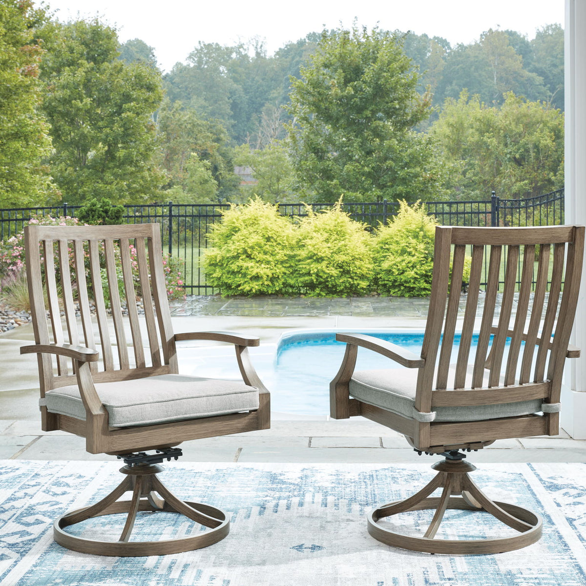 Two brown swivel patio chairs with gray cushions and slatted backrests on deck