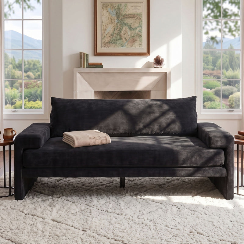 Dark gray upholstered 3-seater sofa with wide armrests, styled with light pillows.