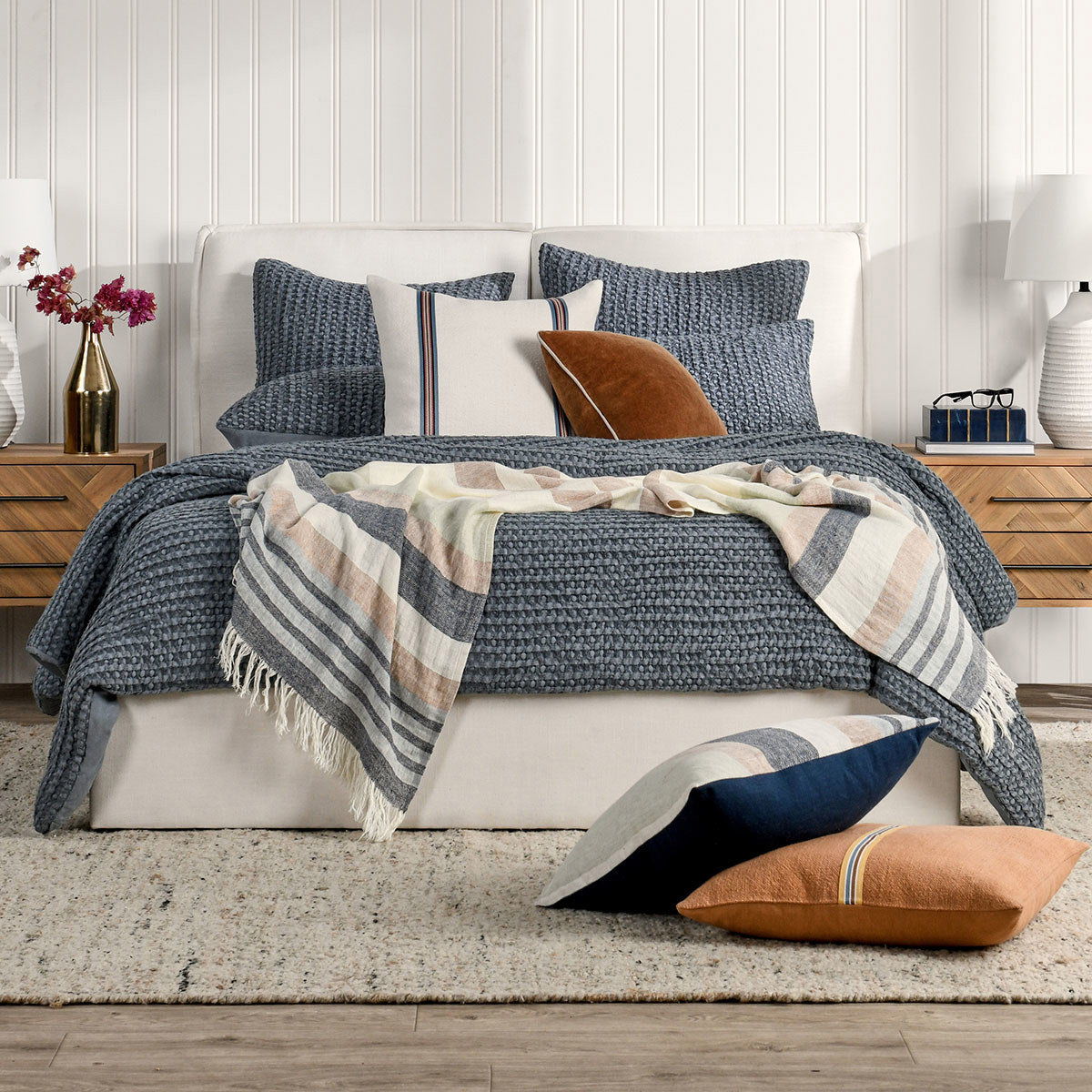 Blue quilt with textured stitch pattern, styled on a bed with decorative pillows.