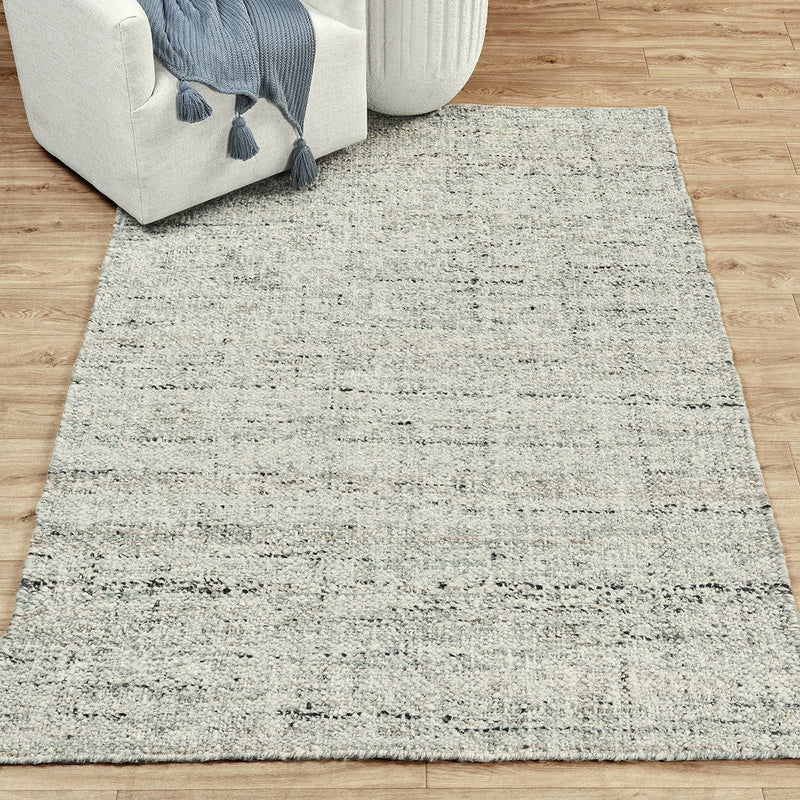 Flatweave area rug in light gray with distressed speckled texture and fringed edges