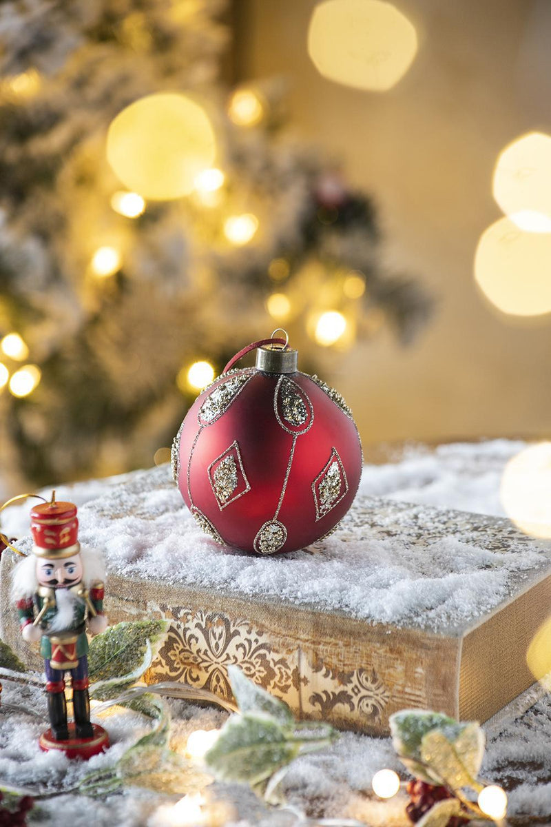Red and gold decorative Christmas ball ornament on snowy wood block with nutcracker figurine