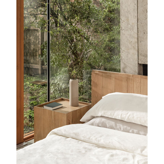 Natural oak king bed with slatted headboard, white pillows and wood side table