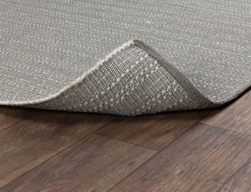 Pebble gray indoor/outdoor rug corner with flat weave texture and bound edge.