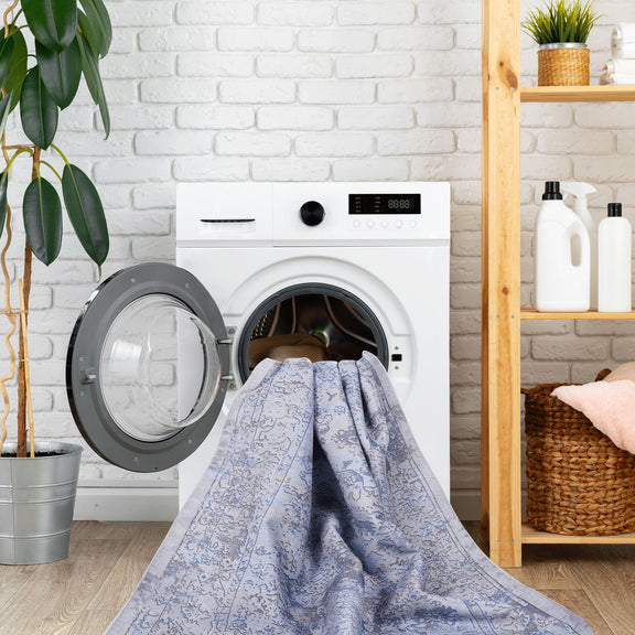 Washable area rug draped over washing machine, light blue with cream abstract pattern