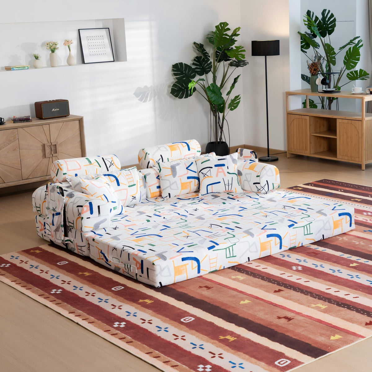 White sleeper sofa bed with colorful icon-pattern cushions, folded ready for sitting