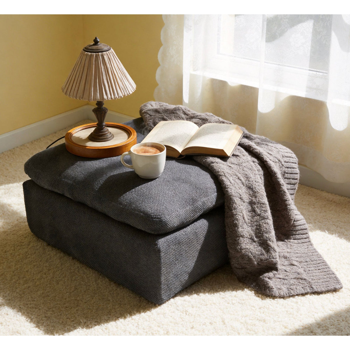 Dark gray upholstered ottoman with rounded lid and visible corner seam