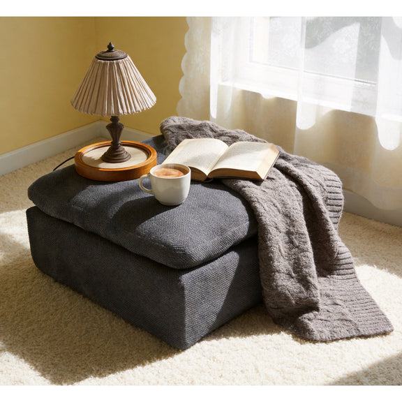 Dark gray upholstered ottoman with rounded lid and visible corner seam