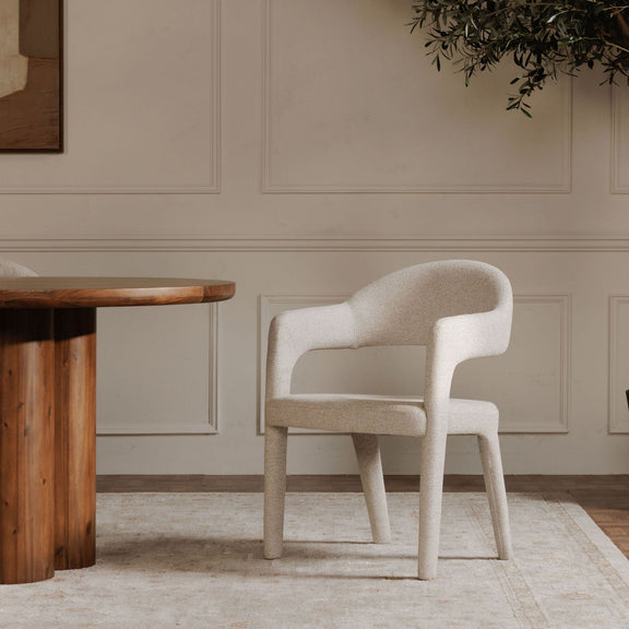 Beige dining chair showing its curved upholstered back, arms, and tapered legs
