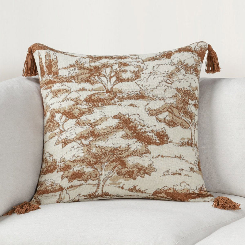 Clay forest-print throw pillow with tassels on a sofa, beige and rust-brown trees.