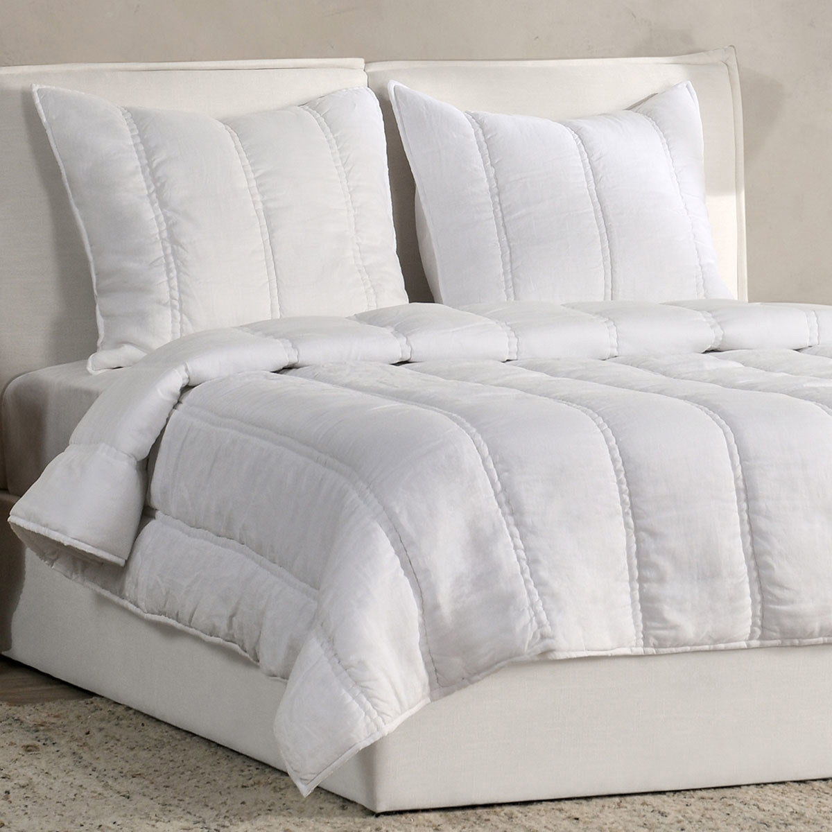 White quilt and pillows set with stitched channels, folded over a bed