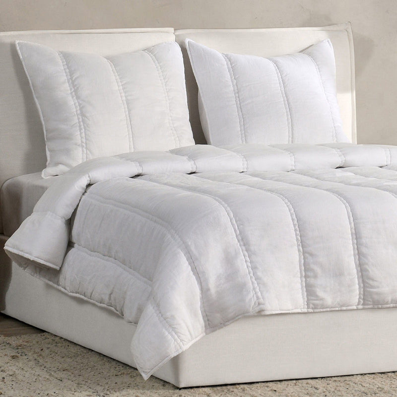 White quilt and pillows set with stitched channels, folded over a bed