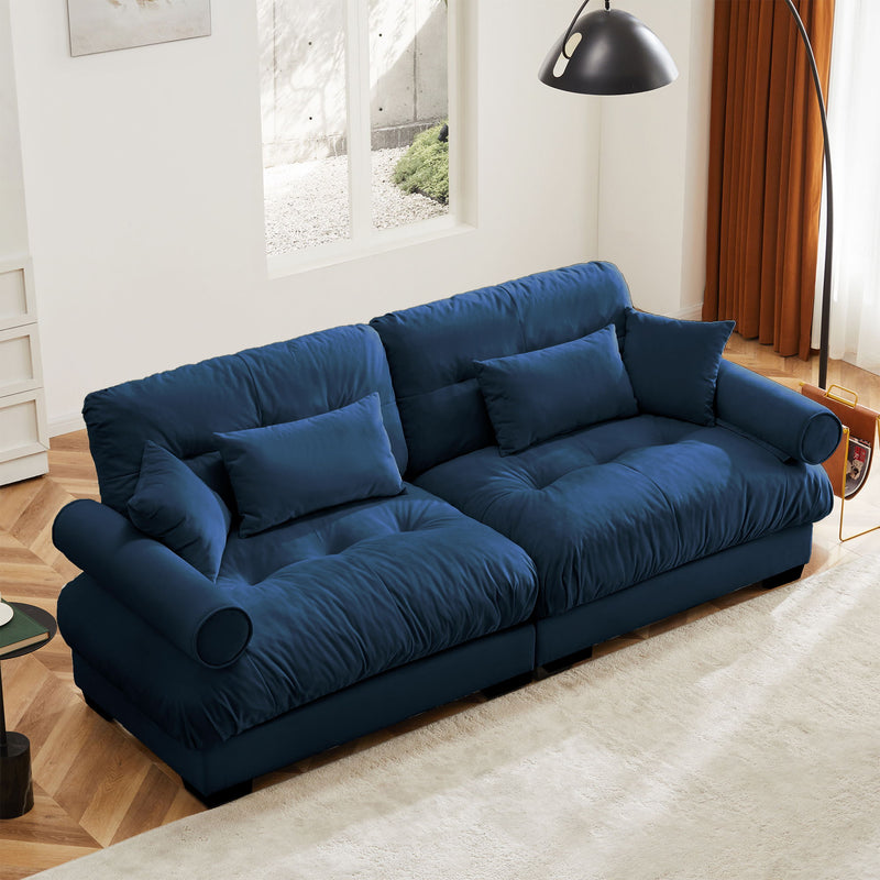 Blue upholstered sofa with tufted cushions and back throw pillows, rounded bolster arms