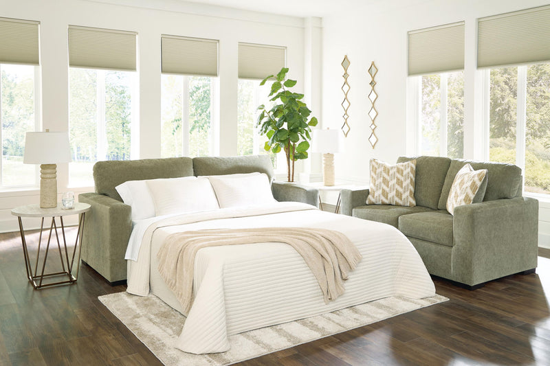 Green sofa sleeper with bed extended, white bedding and striped throw blanket