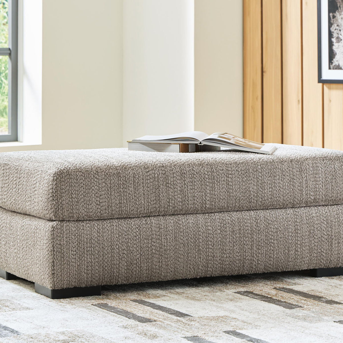 Gray upholstered ottoman with stitched cushion and black base feet