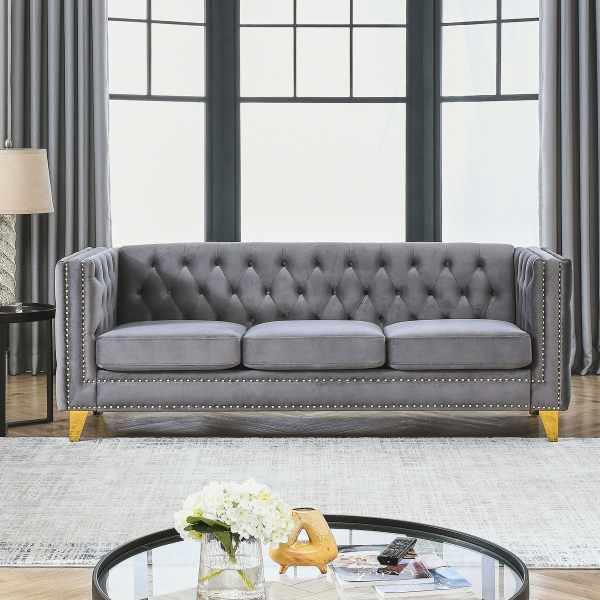 Dark gray button-tufted sofa with nailhead trim, three seat cushions, and gold legs