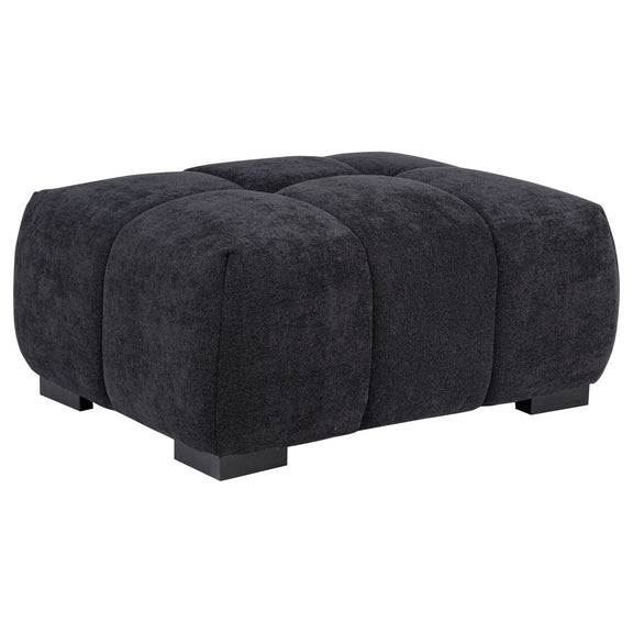 Dark gray rectangular upholstered ottoman with tufted sections and low black legs.