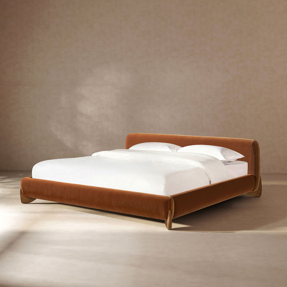 Warm orange-brown upholstered platform bed with low headboard and slatted base