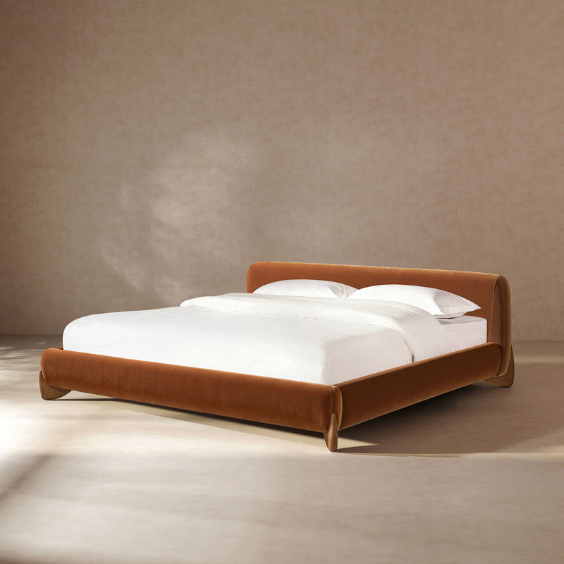 Warm orange-brown upholstered platform bed with low headboard and slatted base